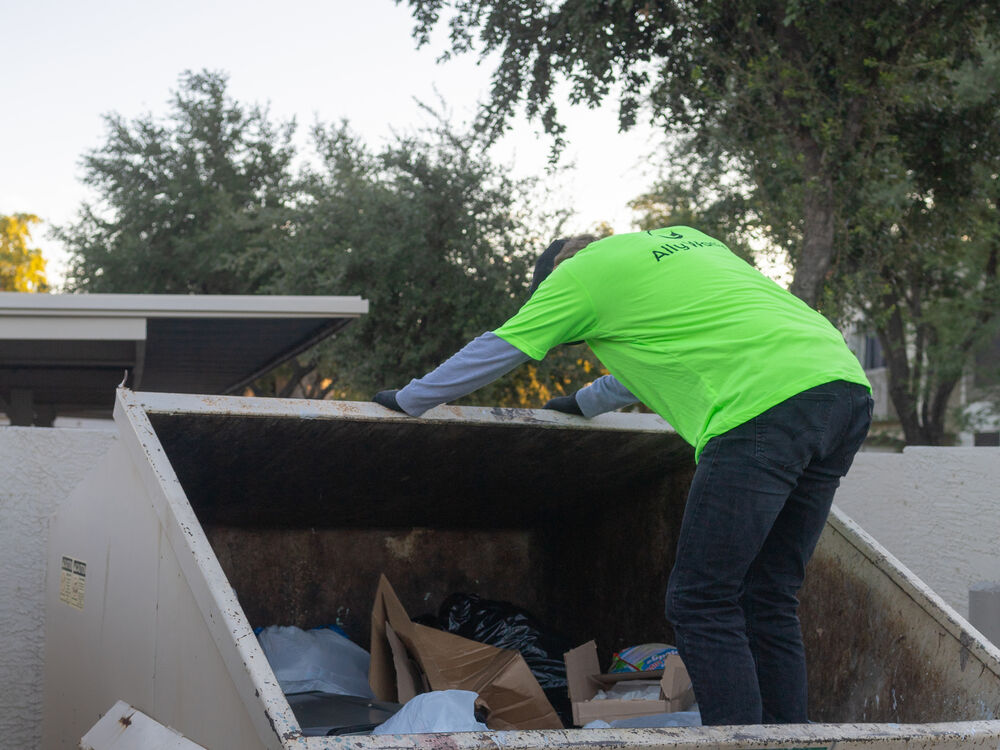 An Ally Waste crew member leans into an open dumpster to spread out the load