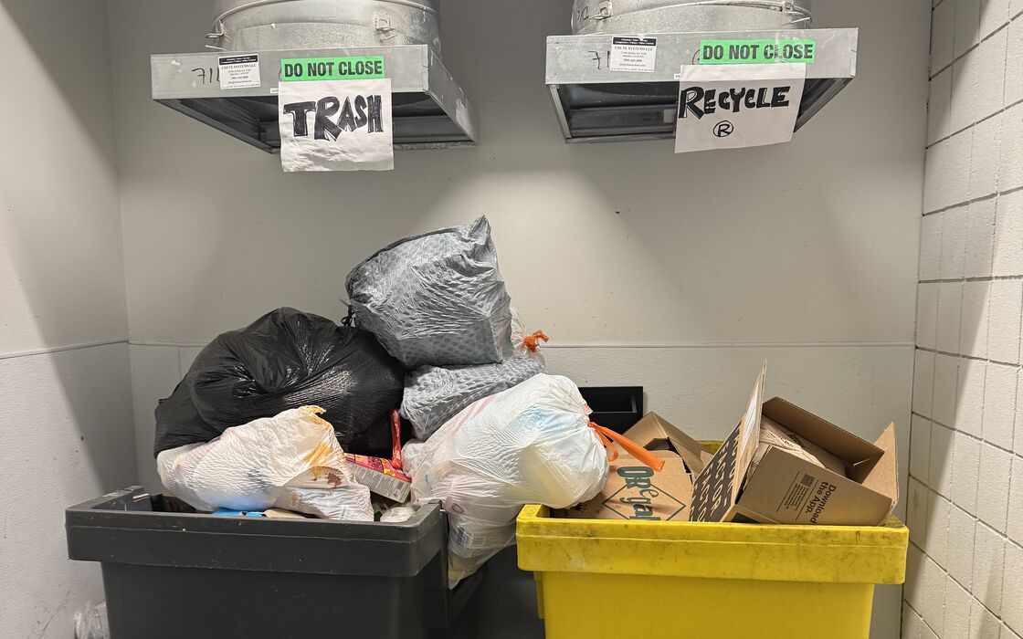 A chute room where the trash and recycling carts under the labeled chutes are heaped with bags and boxes