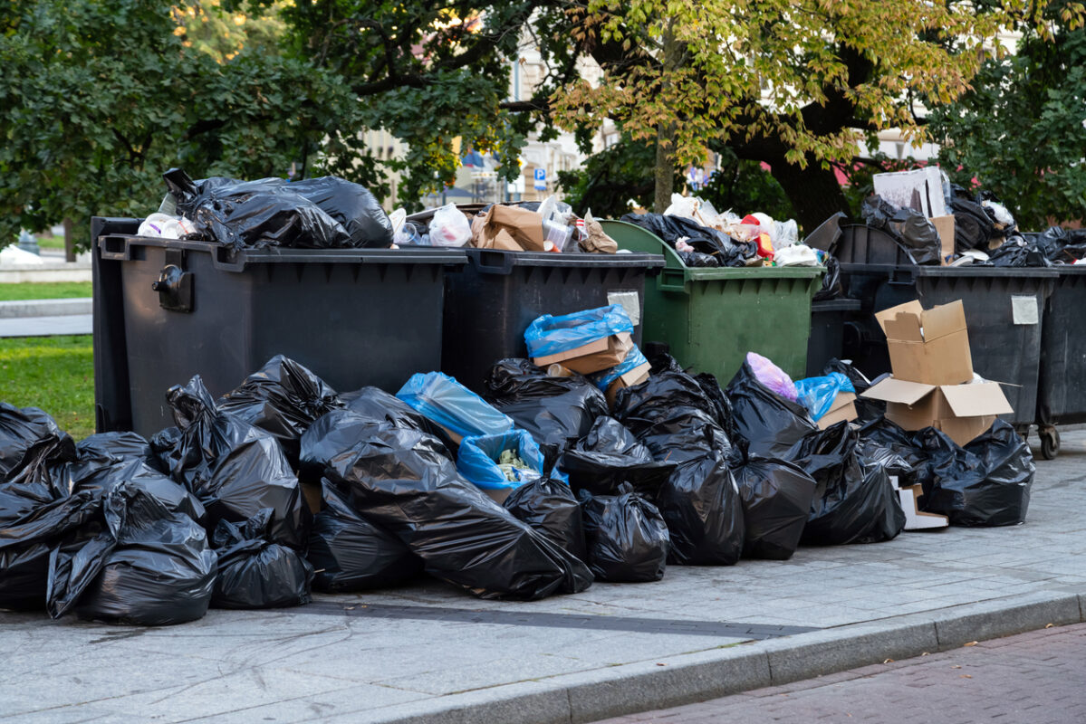 Huge garbage piles next to the dumpster after city fair Stacks of litter bags overflow trash cans after festival in a city | Ally Waste